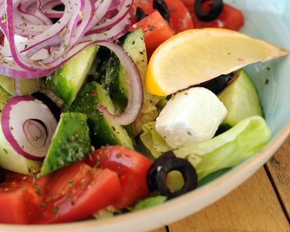 A vibrant bowl of Greek salad with fresh vegetables, feta cheese, and a lemon slice.